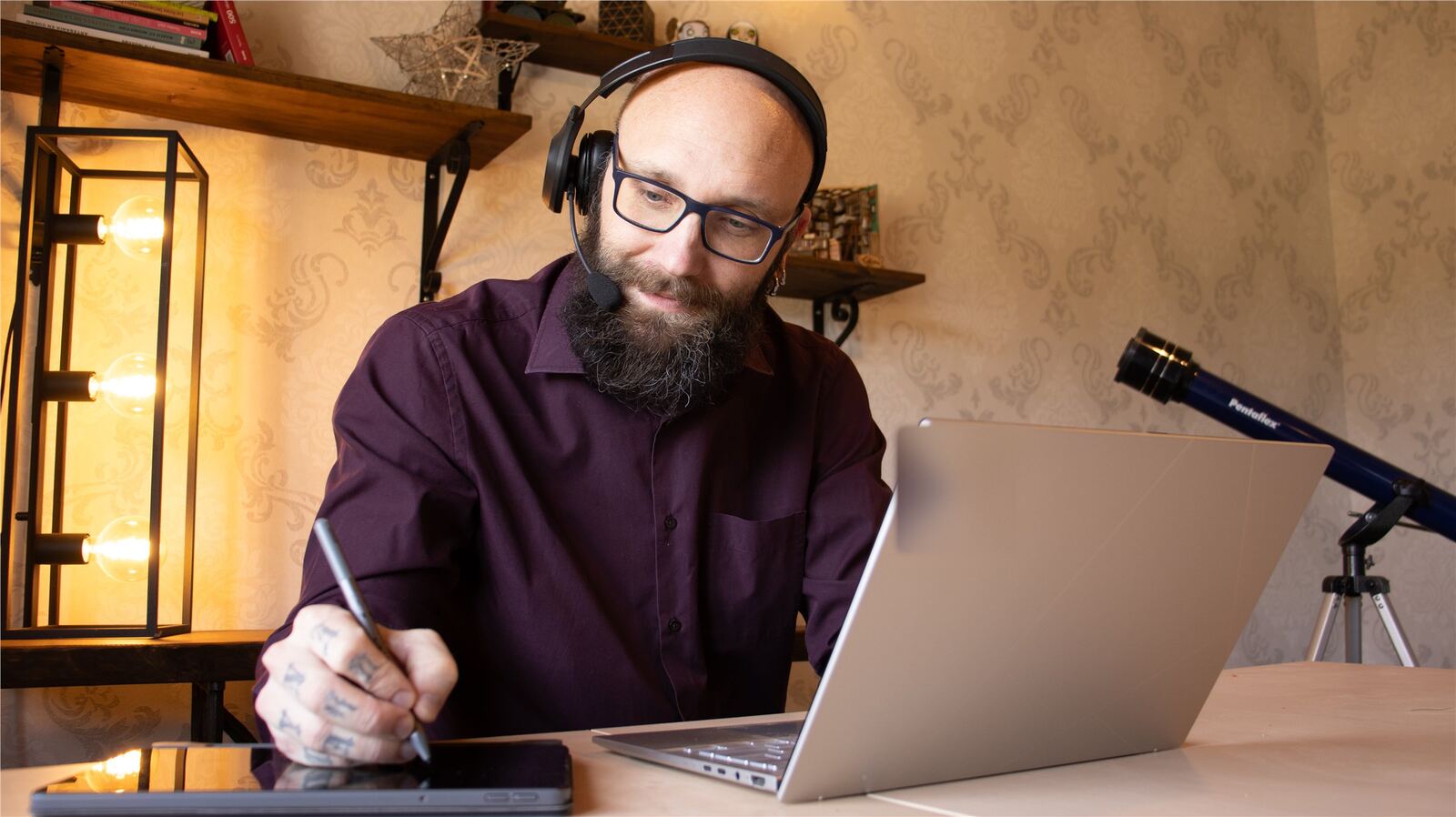 Björn working at a desk with a laptop, headset, drawing tablet, and warm studio light